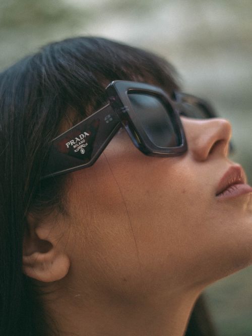 Free Side view close-up of a woman wearing fashionable Prada sunglasses, emphasizing style and elegance. Stock Photo