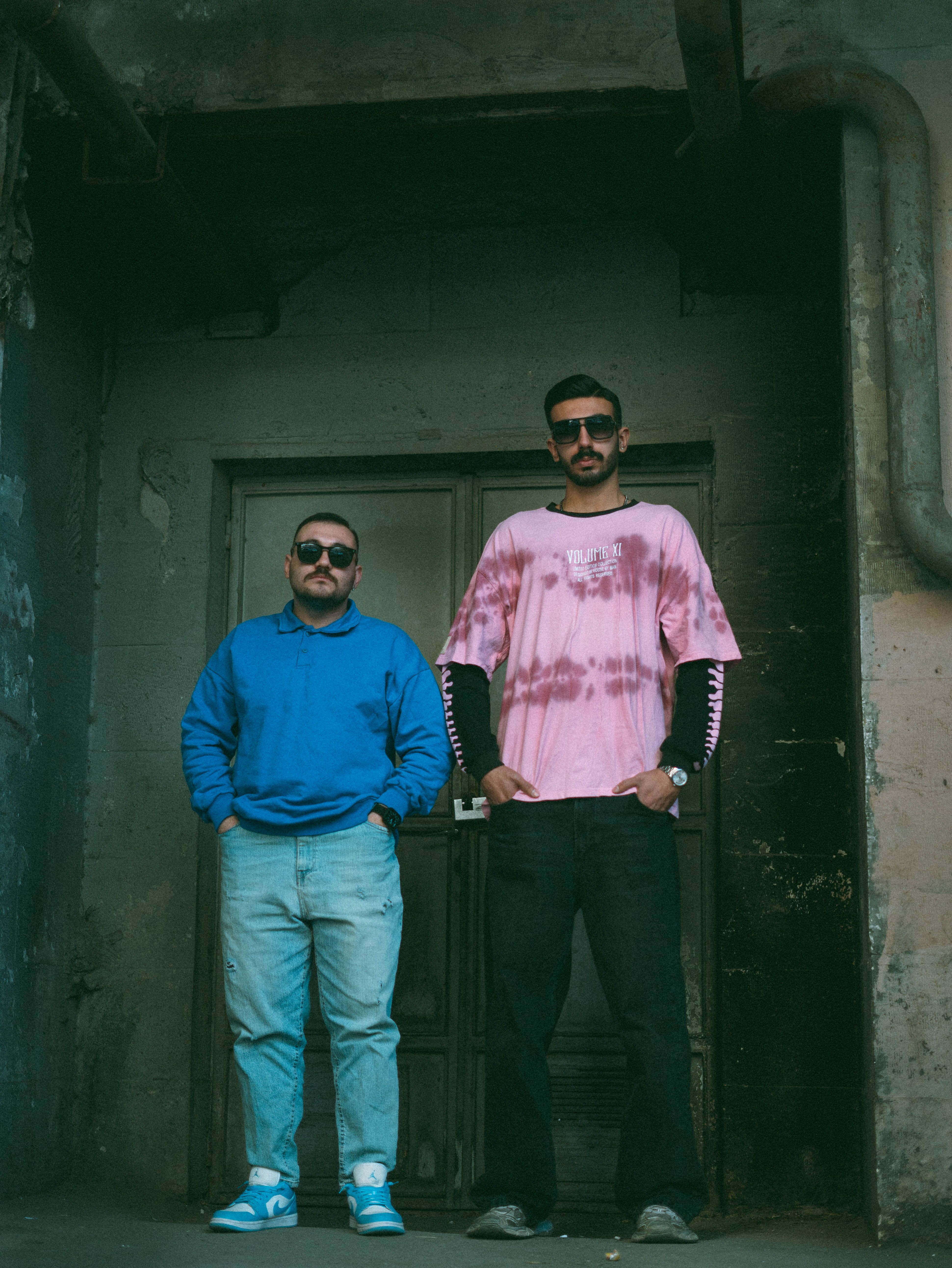 Two men in casual urban wear standing confidently against a gritty backdrop.