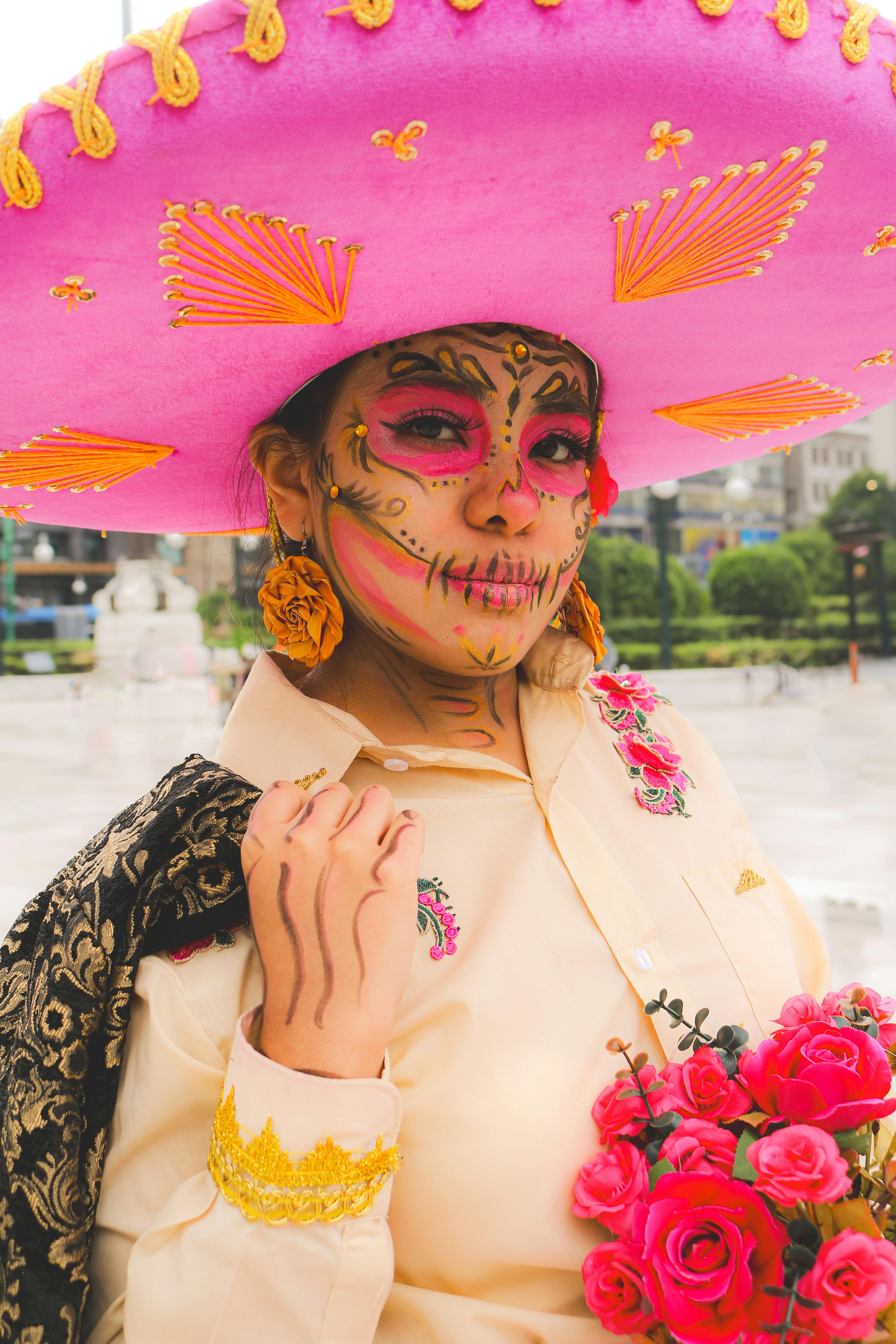 Vibrant portrait of a woman in Dia de los Muertos attire with face paint and pink sombrero.