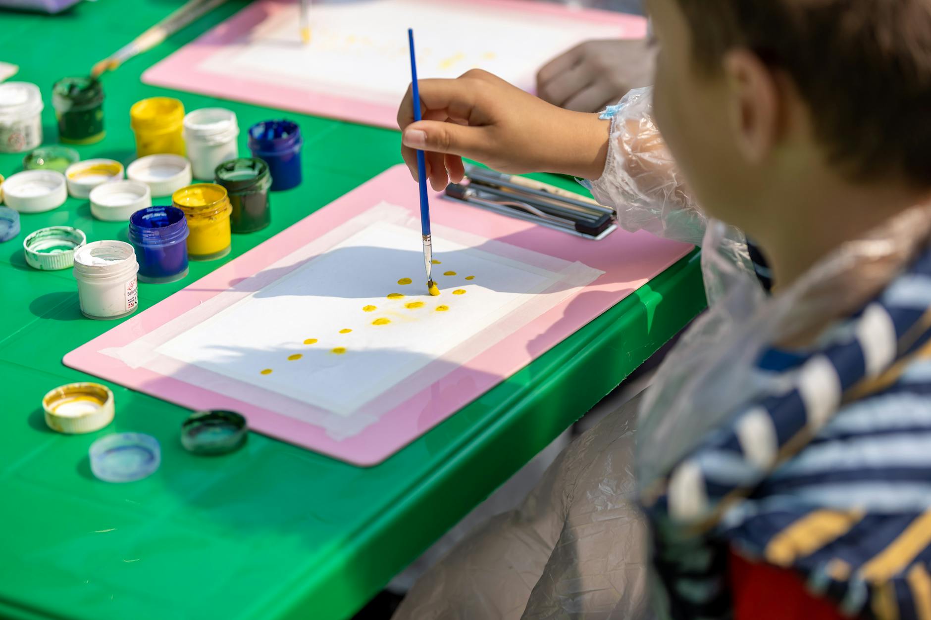 A child painting outdoors using colorful paints and brushes on a sunny day. A child painting outdoors using colorful paints and brushes on a sunny day.