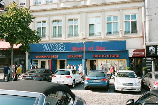 Lively street scene in Hamburg with adult-themed shops and cars parked outside.