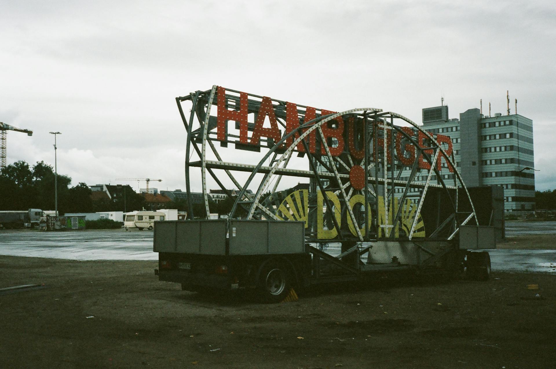Large carnival sign on truck in urban outdoor setting with building backdrop.