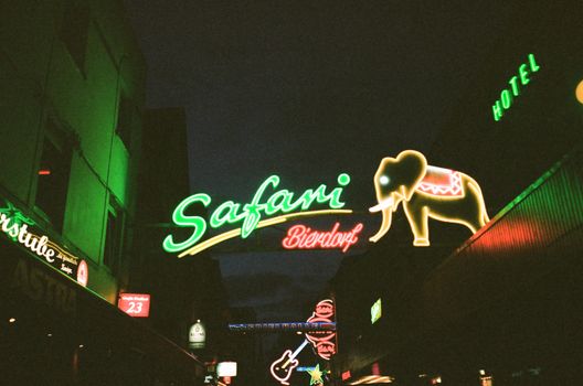 Vibrant neon lights illuminate an urban street scene at night with colorful signage.