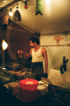 A street food vendor grilling meat at an outdoor market at night.