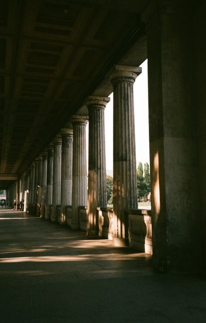 Dramatic view of a column-lined hallway with Greek architectural pillars in warm sunlight.