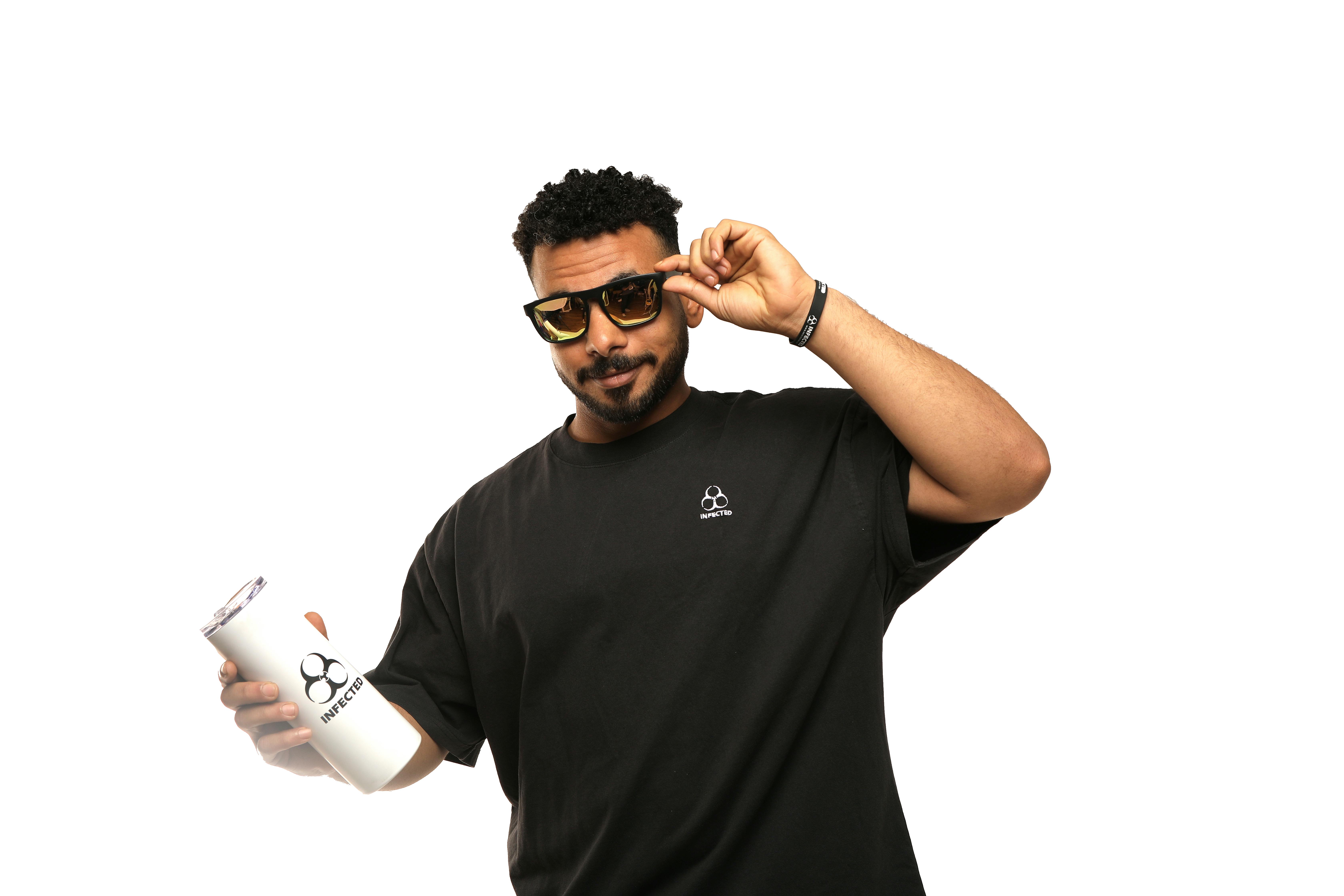 grátis Jovem de óculos escuros e camiseta preta segurando um copo branco sobre um fundo branco. Foto profissional