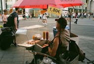 繁华的城区里，一名街头小贩打着红伞卖热狗