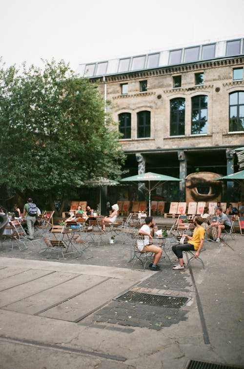 People Sitting Beside Tables Under Parasol Near Building