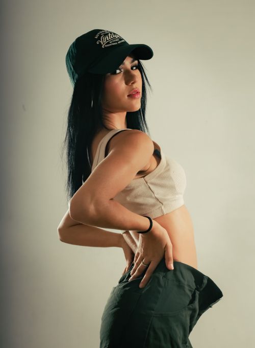 Free Woman posing in casual attire with a baseball cap, high contrast lighting. Stock Photo