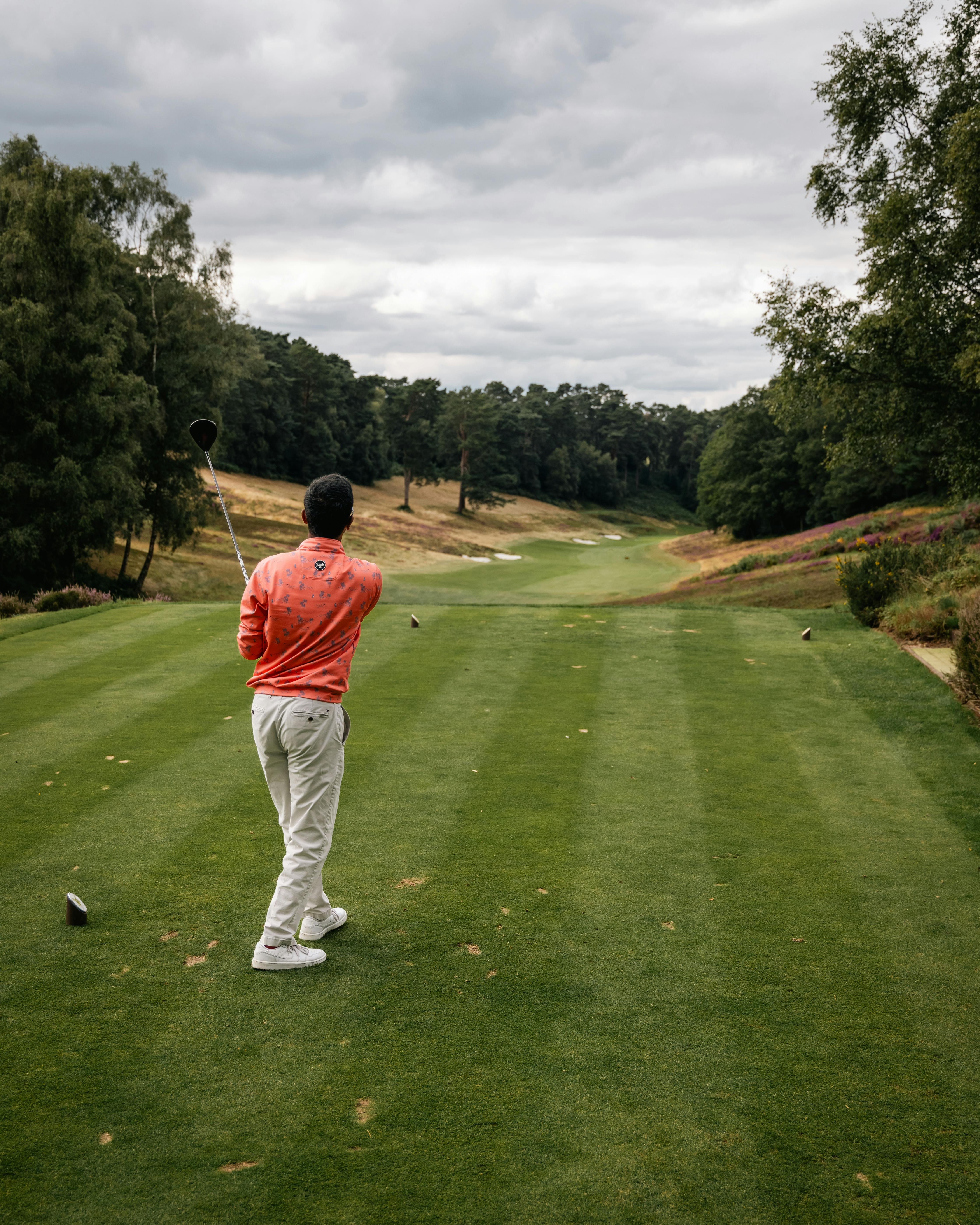 Golfer in action on a scenic golf course in England with cloudy skies.