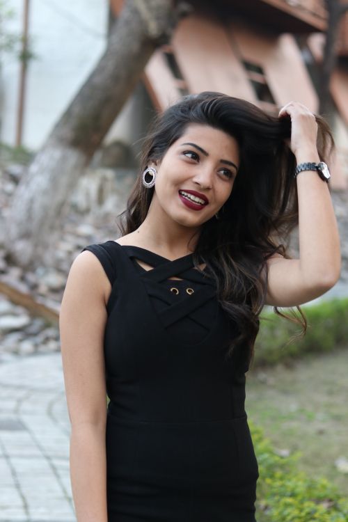 Free A stylish woman in black dress smiles while adjusting her hair outdoors. Stock Photo