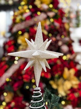 Close-up of a sparkling star ornament with a blurred Christmas tree background.