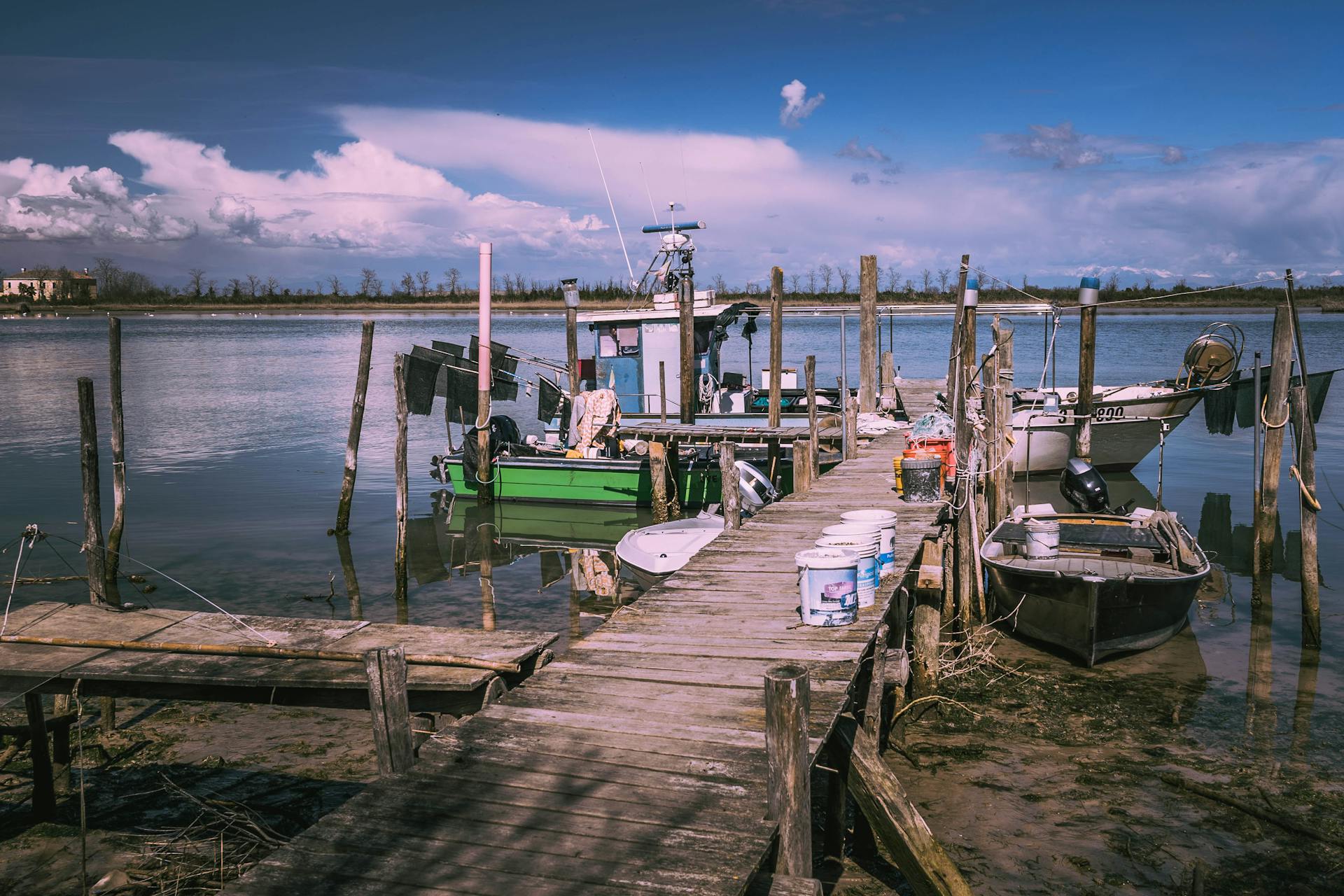 Scenic view of a weathered dock with fishing boats on a calm lake under a bright blue sky.
