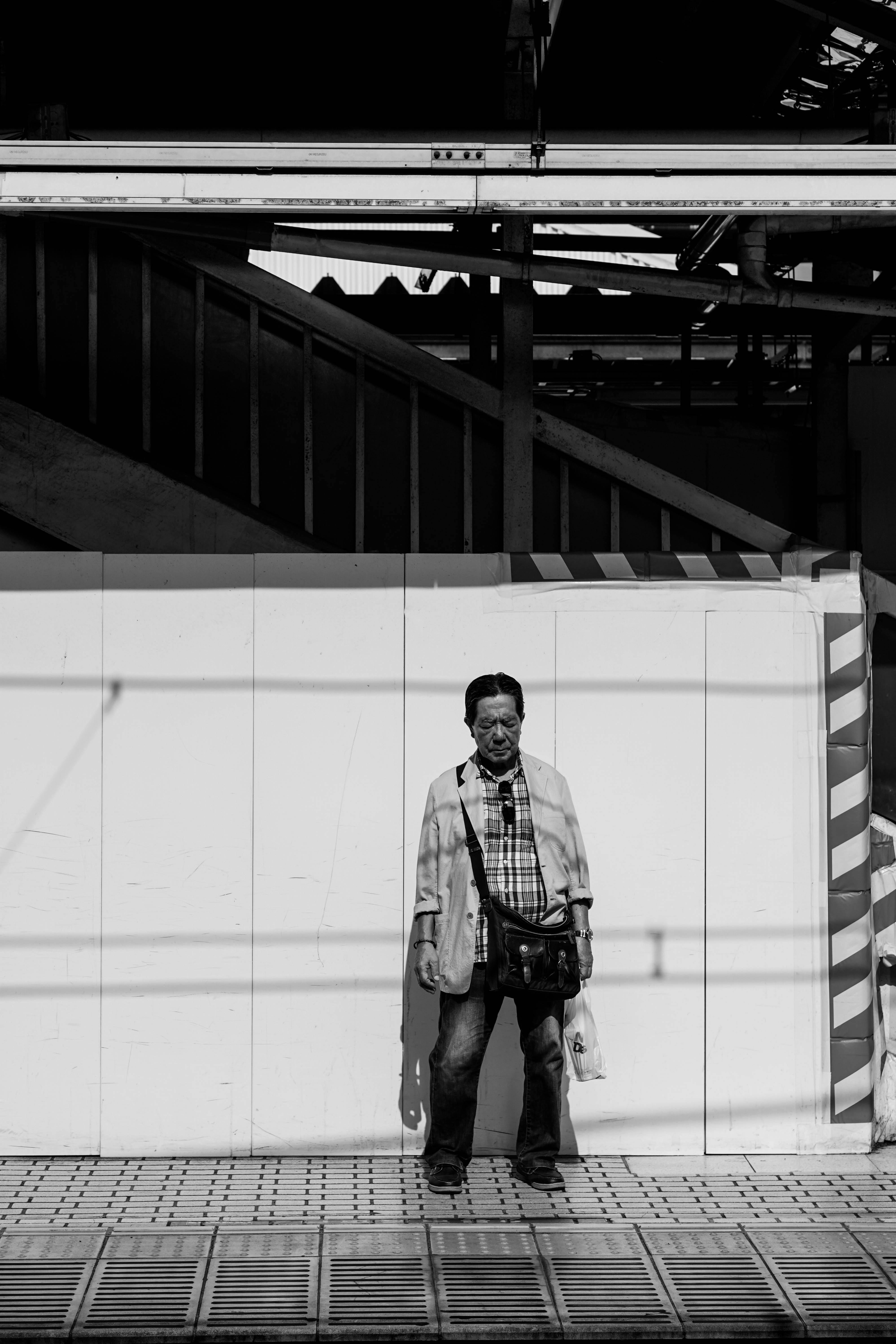 Black and white photo of a man standing against a wall in an urban setting, casting a shadow.