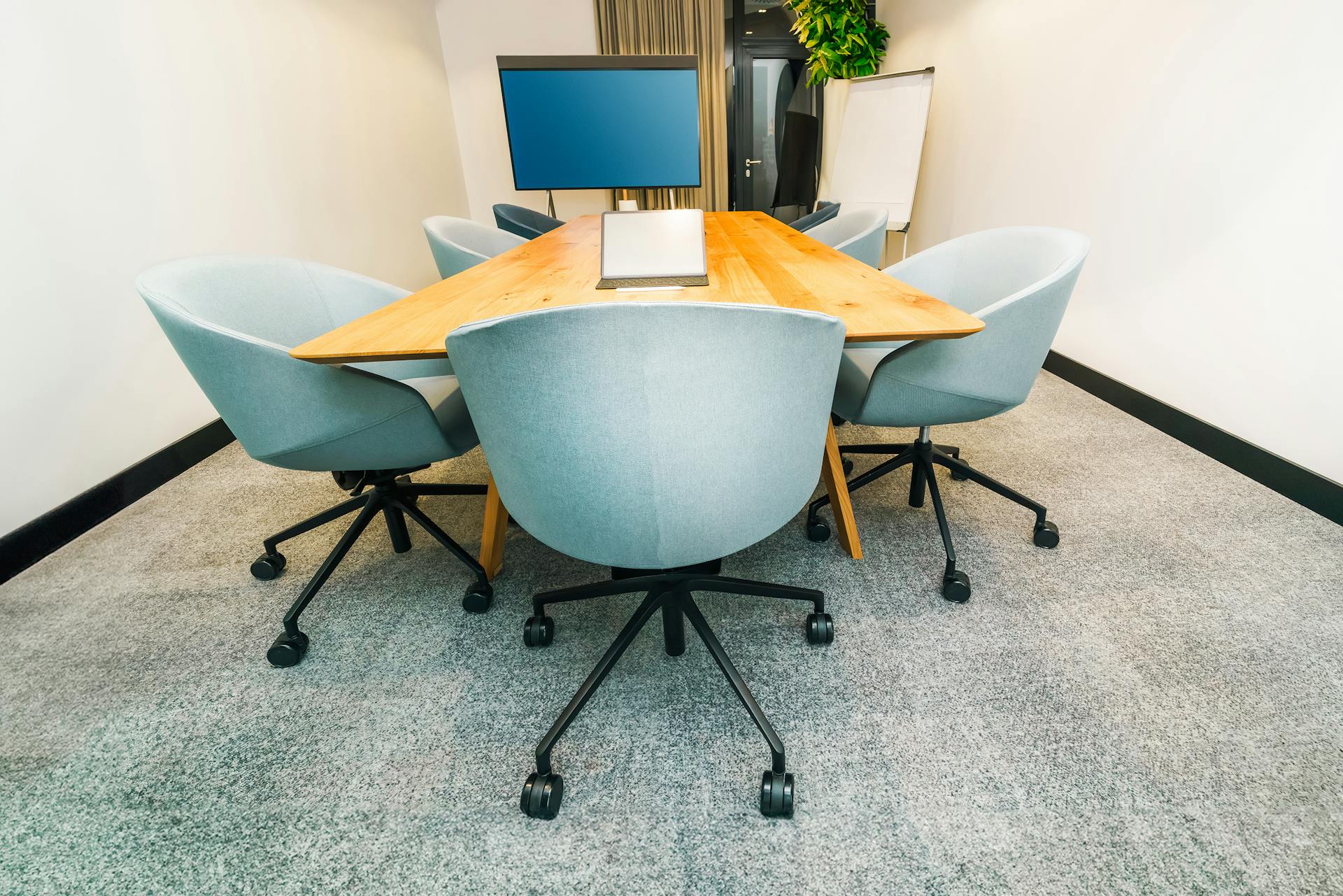 A stylish conference room featuring a triangular table, office chairs, and a TV screen.