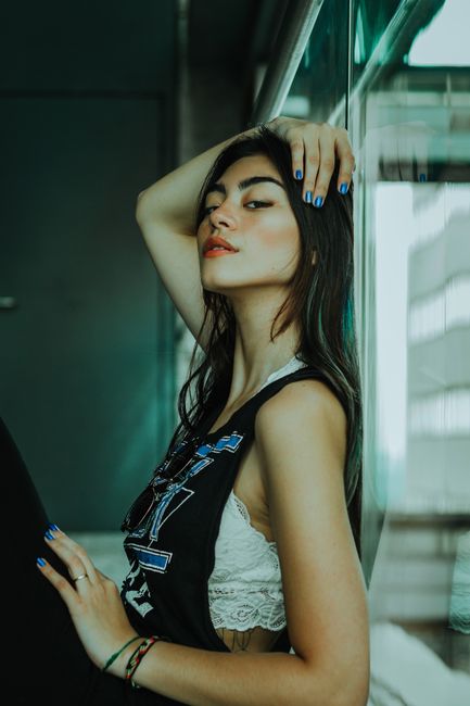 Elegant young woman posing indoors against a window, showcasing modern fashion style.