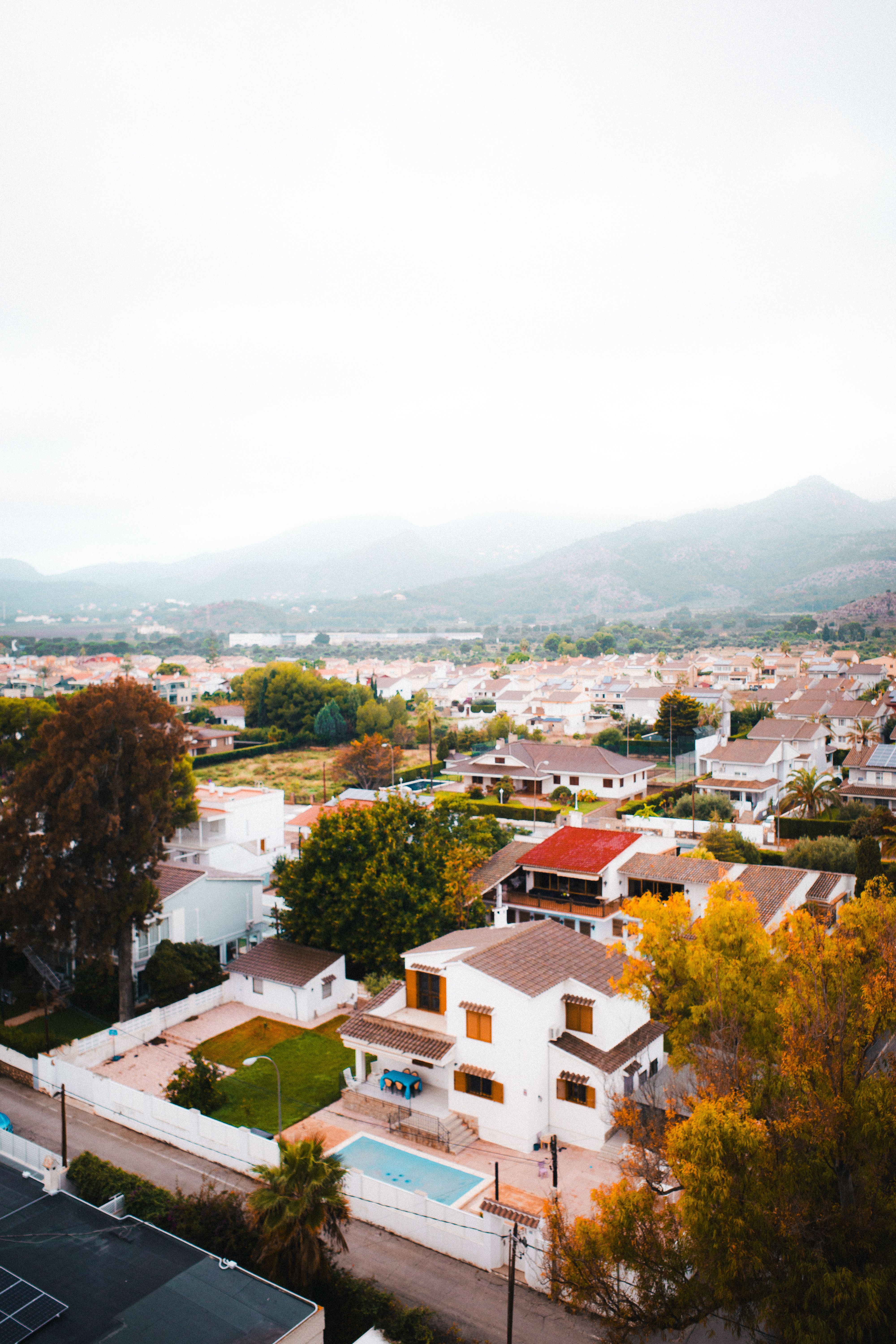 Aerial shot of residential area in Benicàssim, Spain with autumn foliage and scenic mountain backdrop.