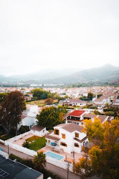 Aerial shot of residential area in Benicàssim, Spain with autumn foliage and scenic mountain backdrop.
