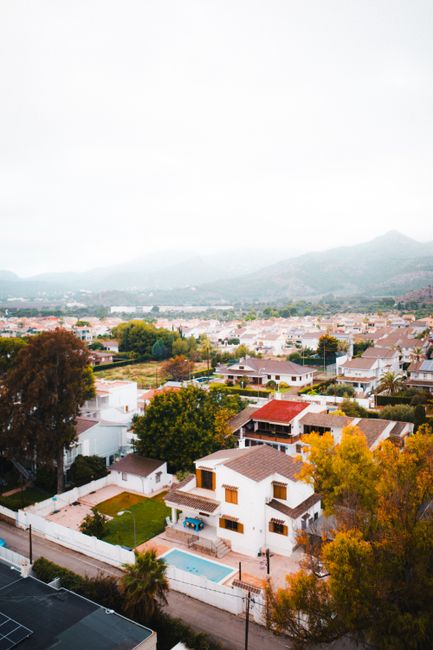 Aerial shot of residential area in Benicàssim, Spain with autumn foliage and scenic mountain backdrop.