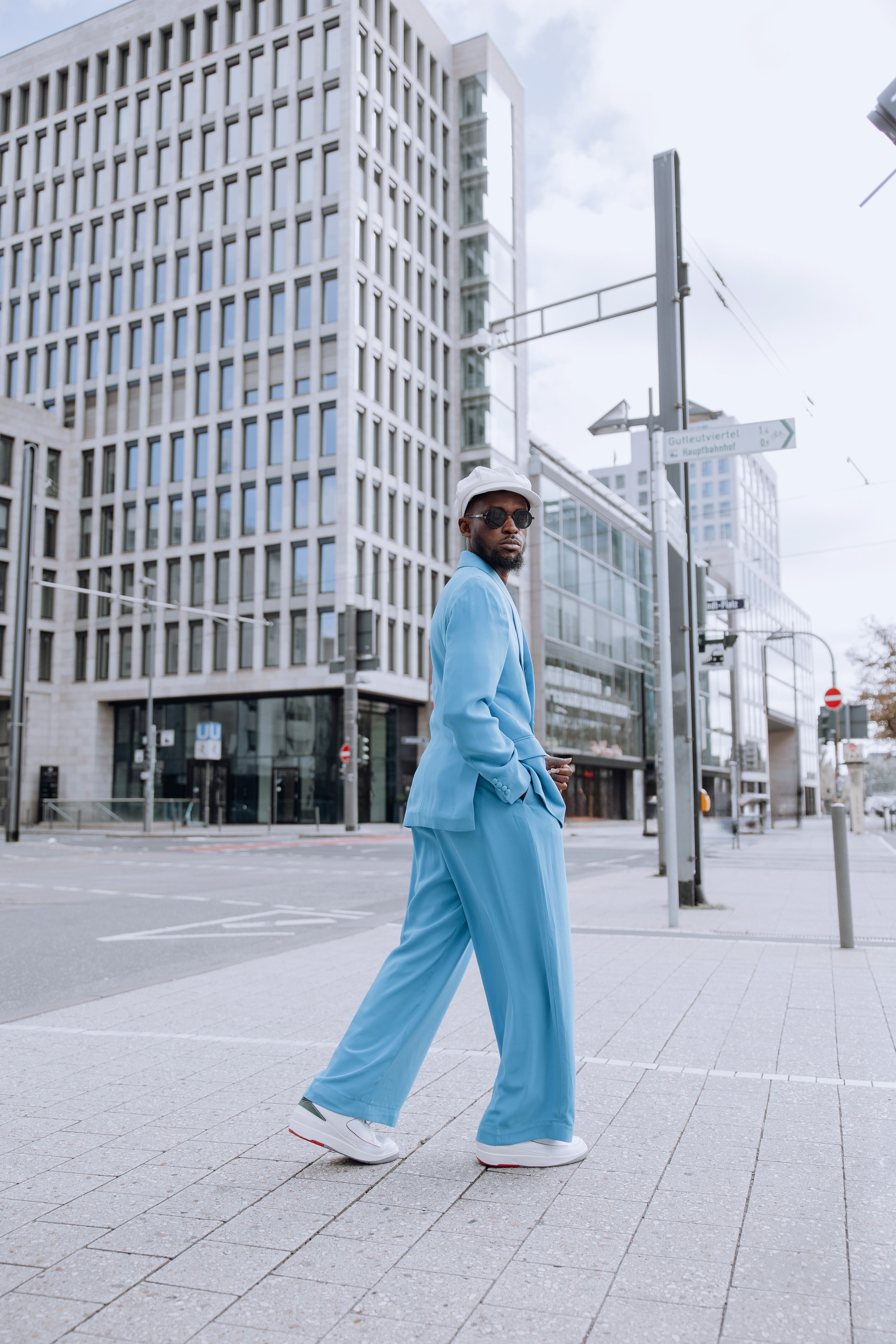 A fashionable man in a blue suit strolls through a modern cityscape, embodying contemporary urban style.