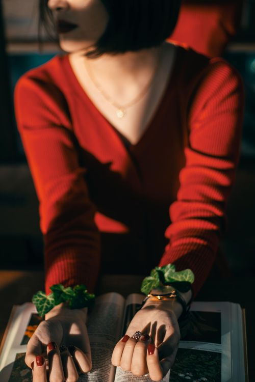 Free Stylish woman in red with book, adorned with green accessories, basking in warm sunset vibes. Stock Photo