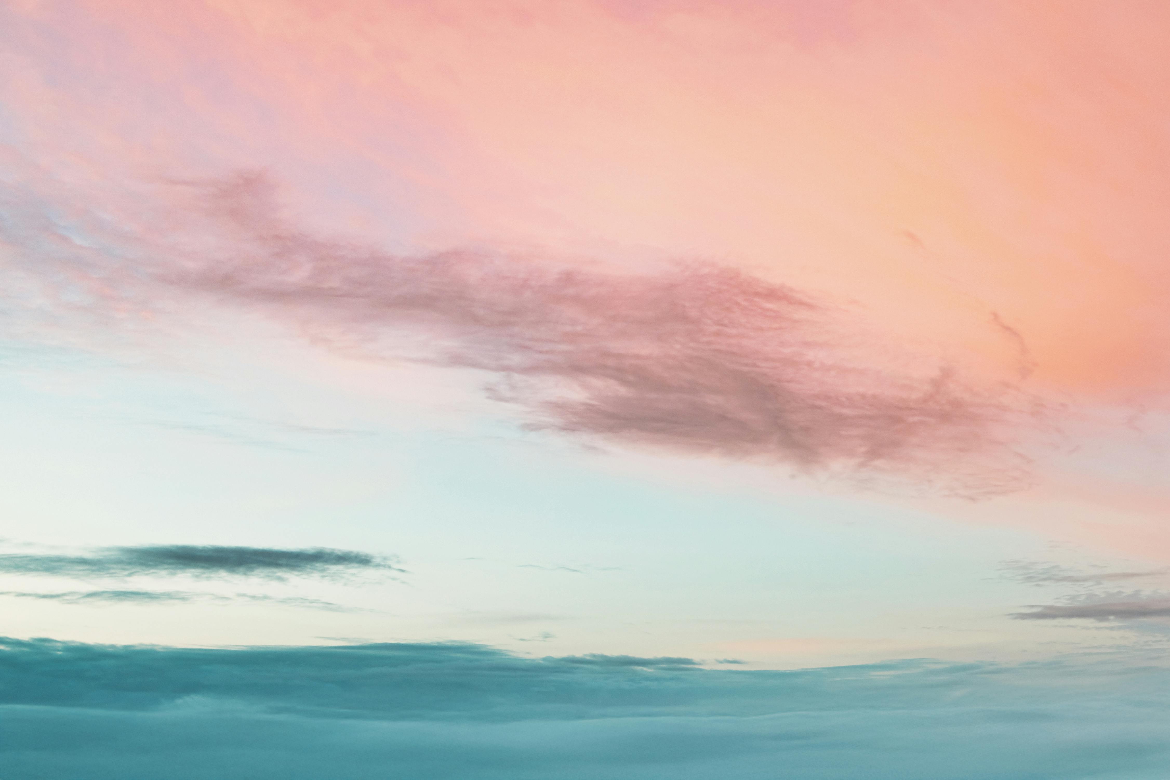 A serene view of a pastel-colored sunset sky with soft clouds blending warm and cool tones.