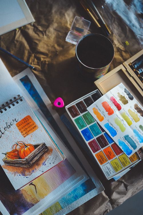 Free Art supplies arranged with watercolors and a painted notebook depicting pumpkins. Stock Photo