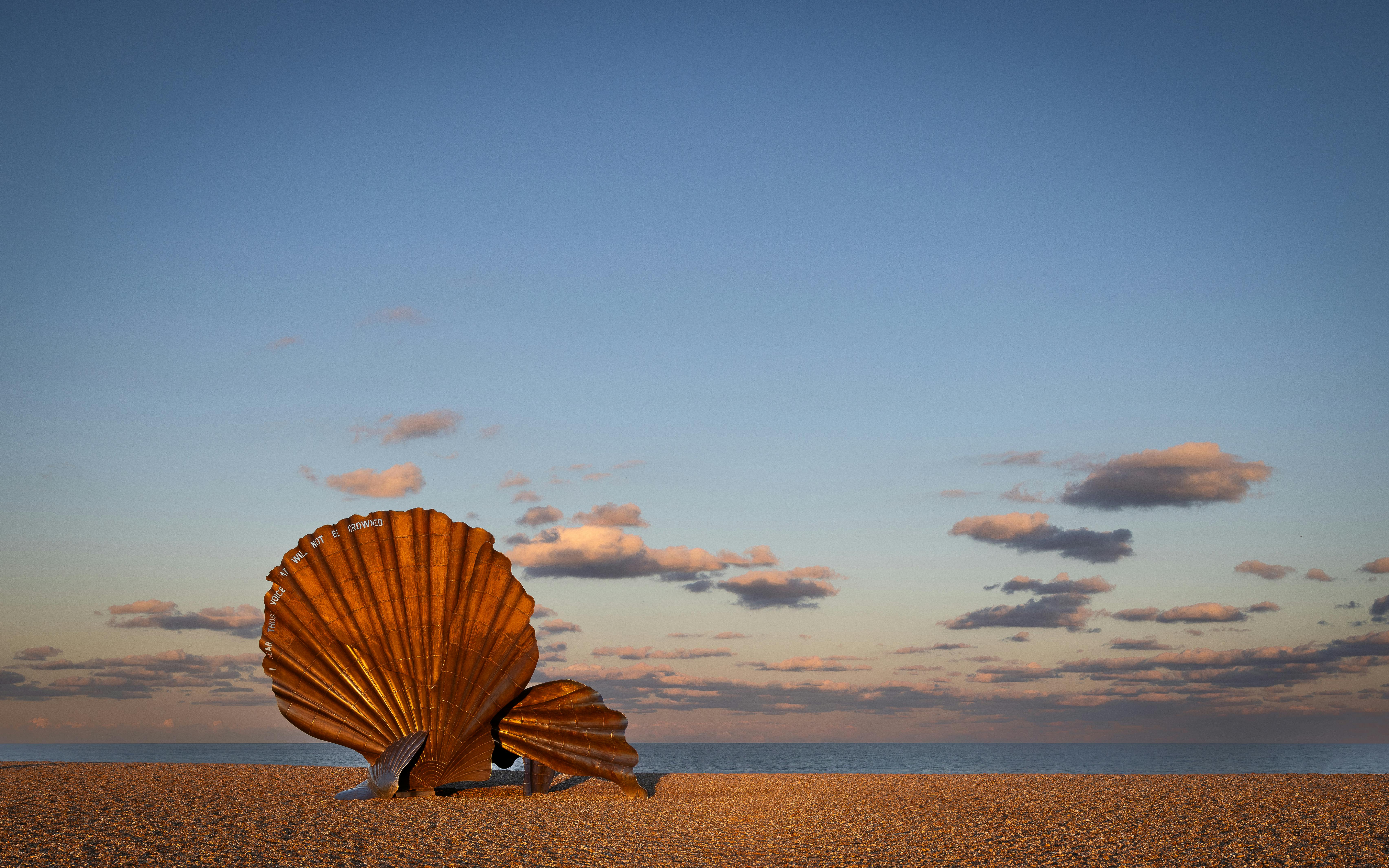 Iconic Scallop sculpture on Aldeburgh beach under a serene sky at sunset.