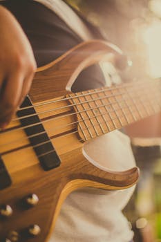A close-up view capturing the aesthetics of a wooden bass guitar being played outdoors, bathed in warm light.