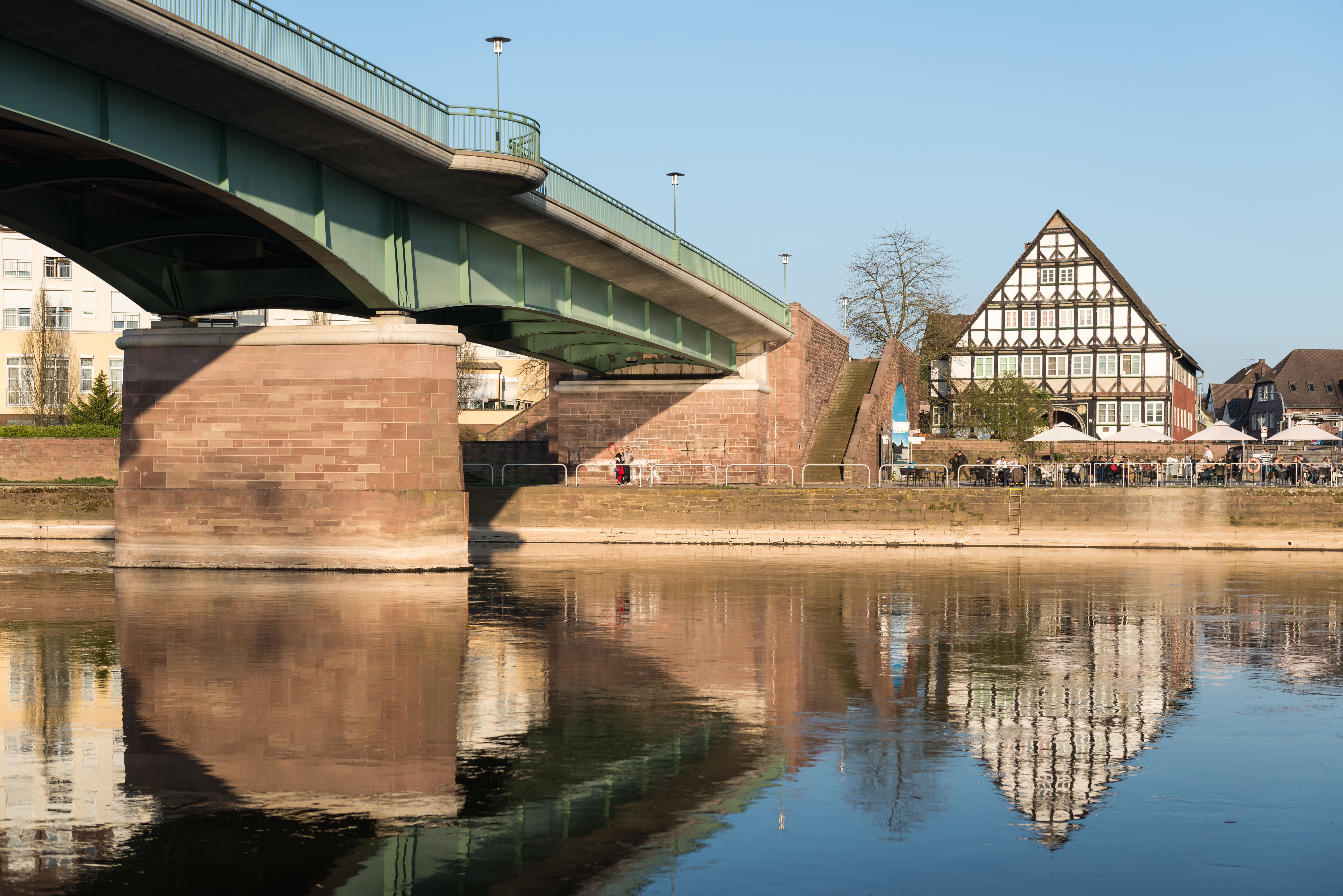 Charming view of Holzminden's riverside with bridge reflection under clear blue skies.