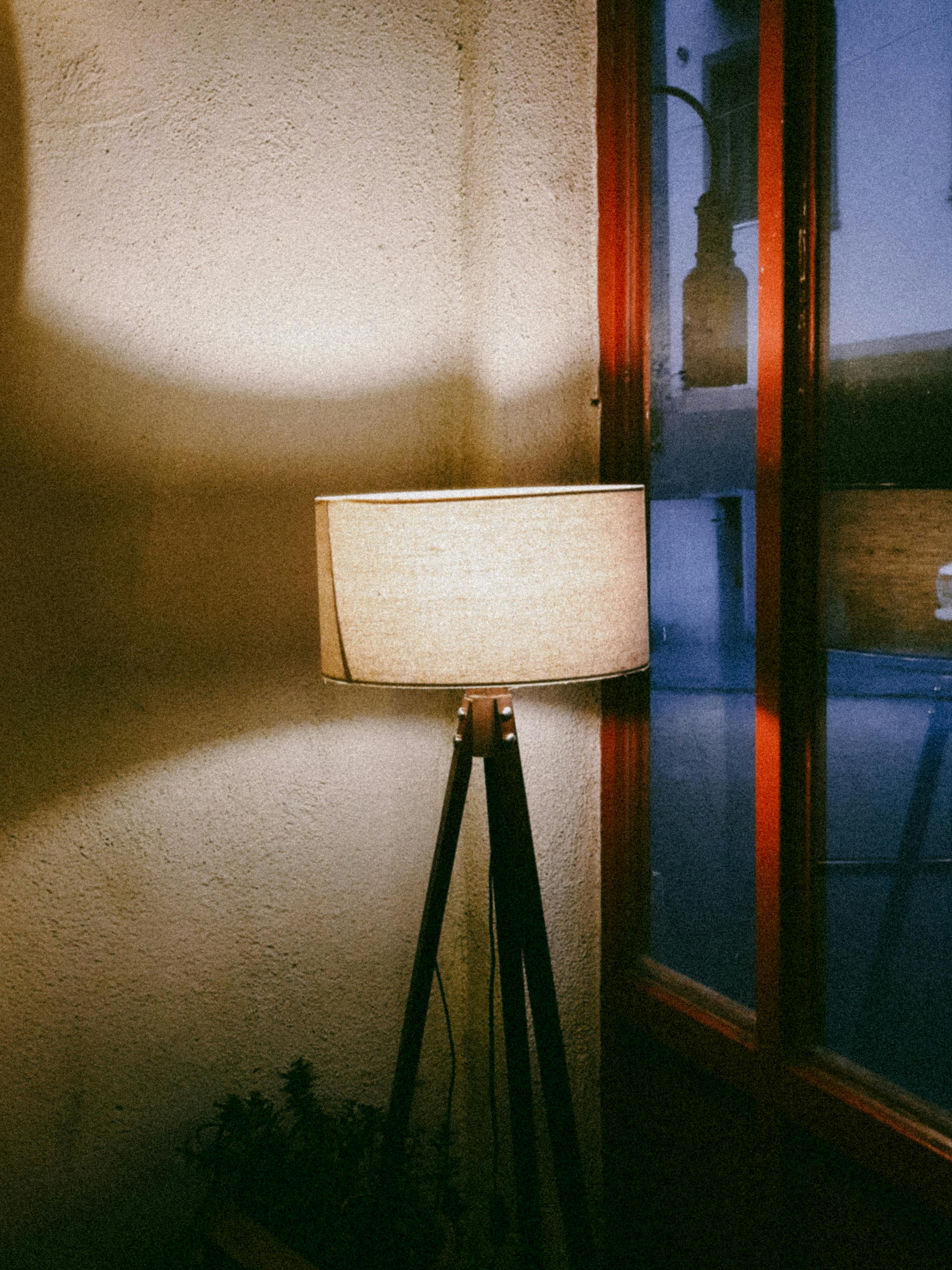 De franc Un llum de peu trípode il·lumina un racó acollidor per una finestra amb la llum del vespre. Foto d'estoc