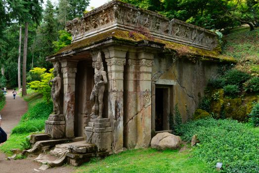 Ancient stone pavilion with statues in a verdant garden landscape.