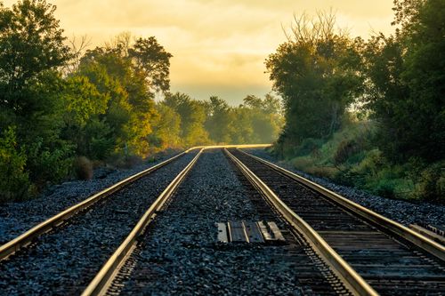 Free Railroad tracks stretch through lush greenery under a golden sunset in Minneiska, MN. Stock Photo