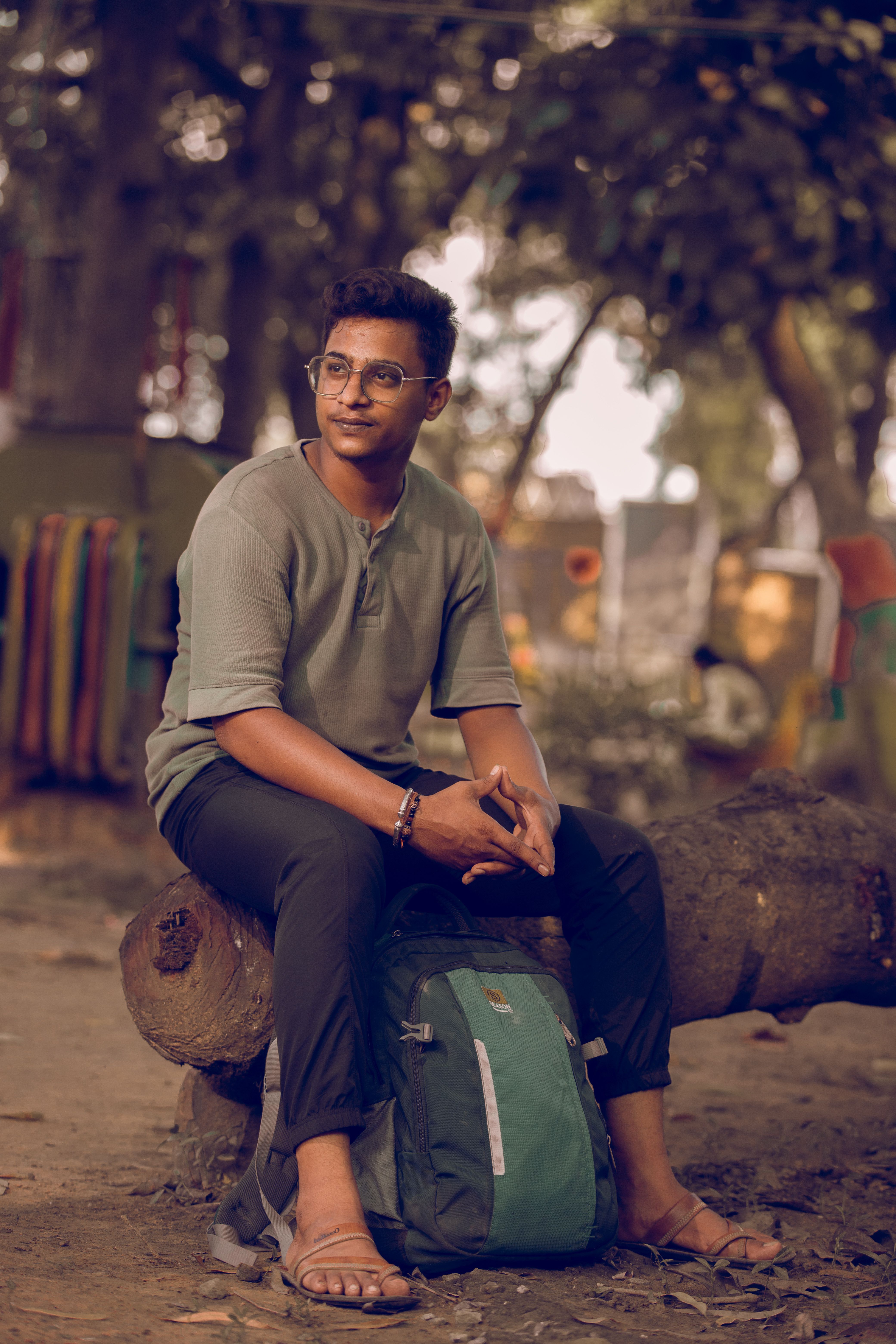 Man sitting on a log with backpack in a park, enjoying nature and reflecting.