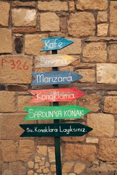 Colorful wooden directional signs against a rustic stone wall in an old village.