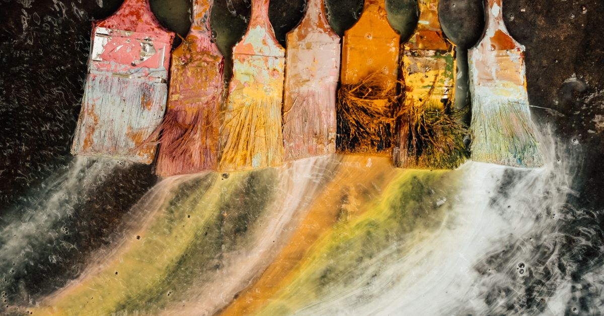 Colorful paint brushes laid on a textured canvas creating an artistic abstract pattern.