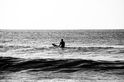 Free Black and white silhouette of a surfer sitting on a board in the ocean, waiting for waves. Stock Photo