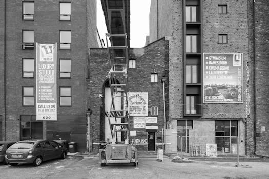 Black and white view of a construction site amidst urban buildings featuring banners and parked cars.