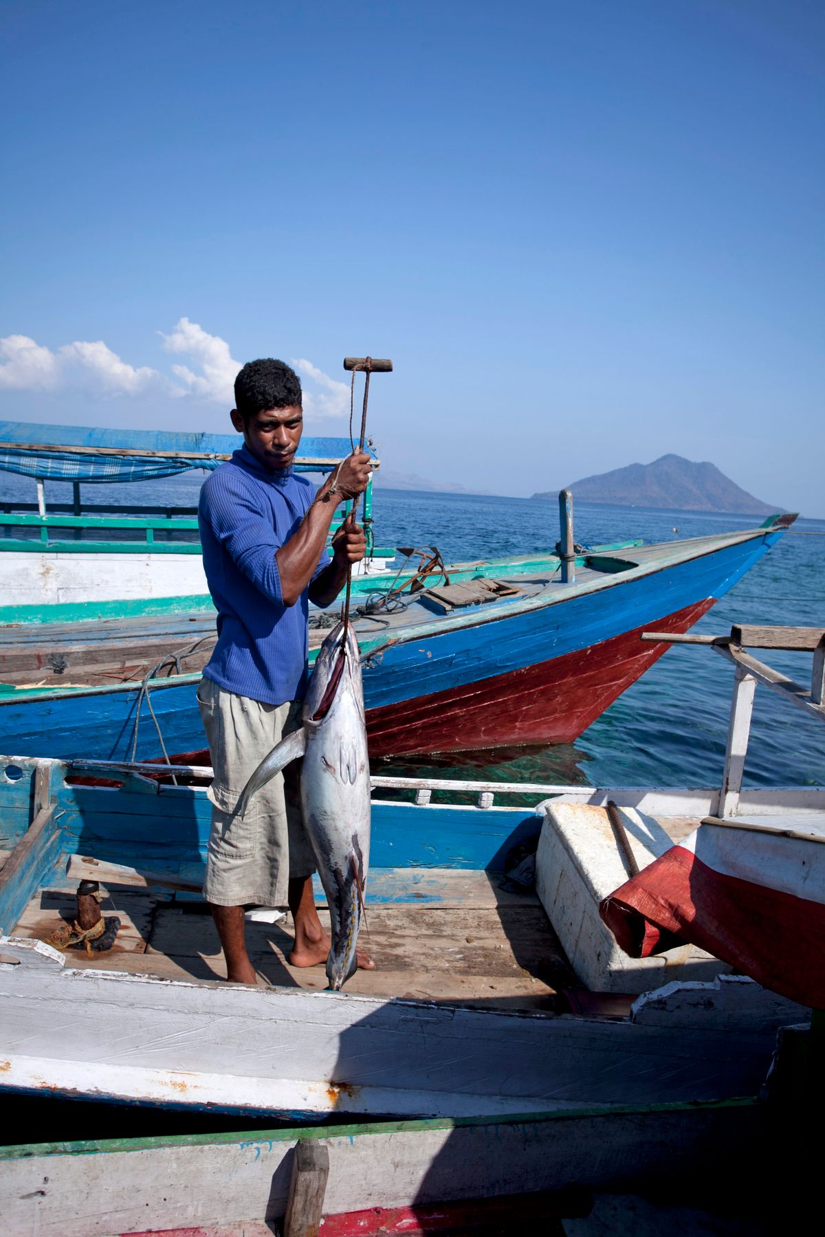 A fisherman holding a large freshly caught tuna on a wooden boat