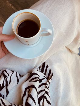A warm cup of coffee held over a zebra print scarf, exuding comfort.