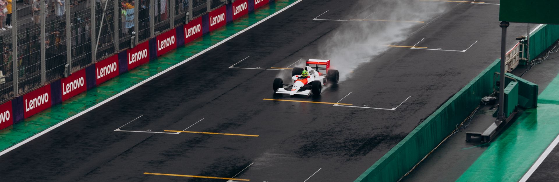 A Formula 1 car speeds through the rain at Interlagos with a cheering crowd.