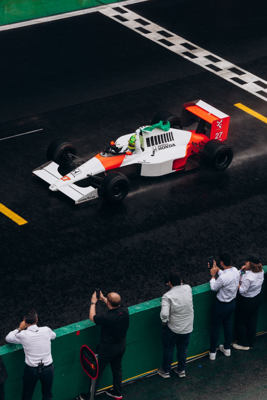 Een vintage Formula 1-auto op een natte racebaan met toeschouwers die het voertuig fotograferen.