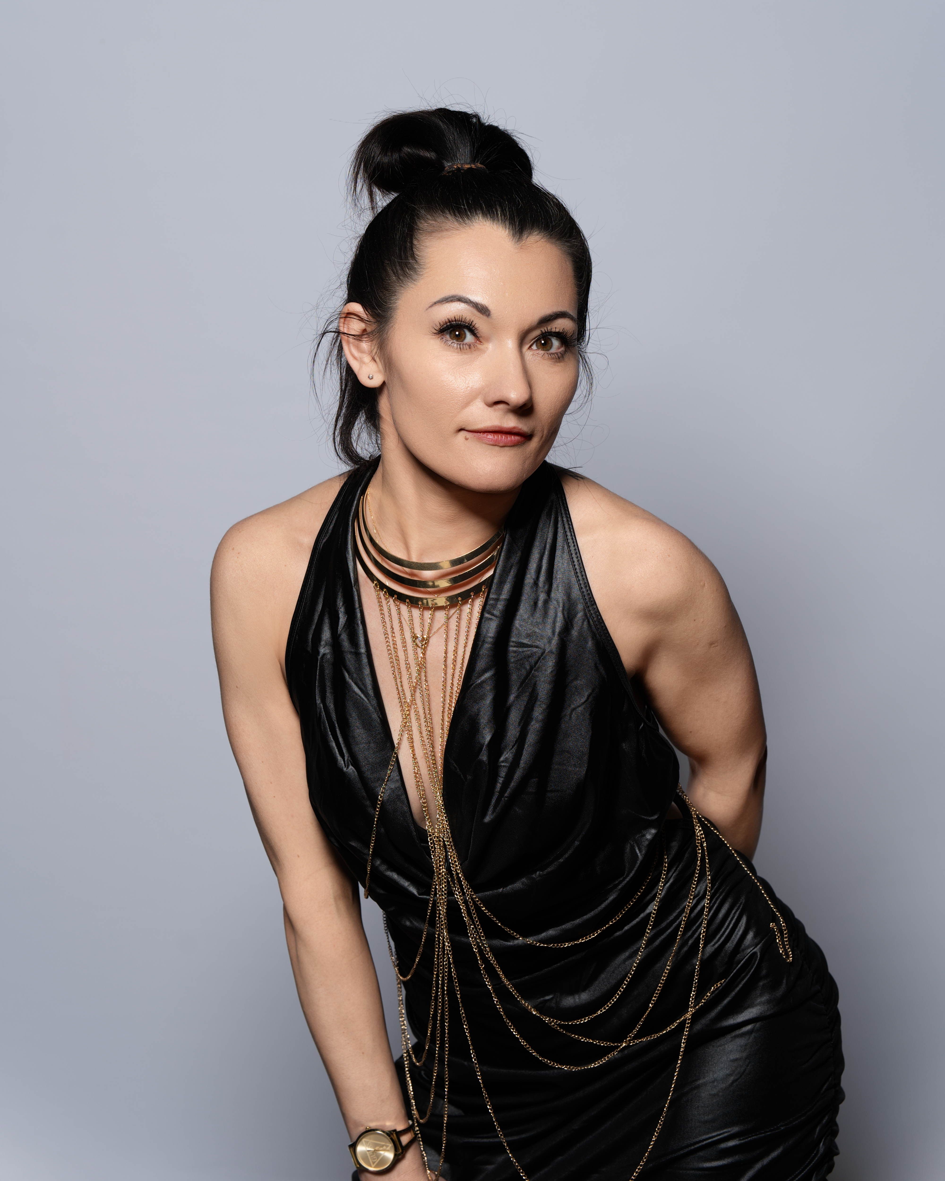 Stylish woman in a black dress adorned with chains, posing confidently indoors.