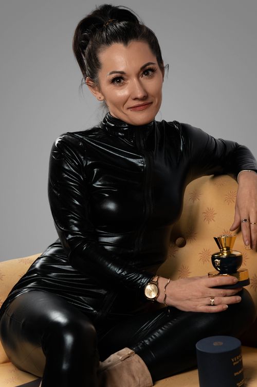 Free Sophisticated woman in a black leather outfit holding a trophy, seated on a stylish couch. Stock Photo