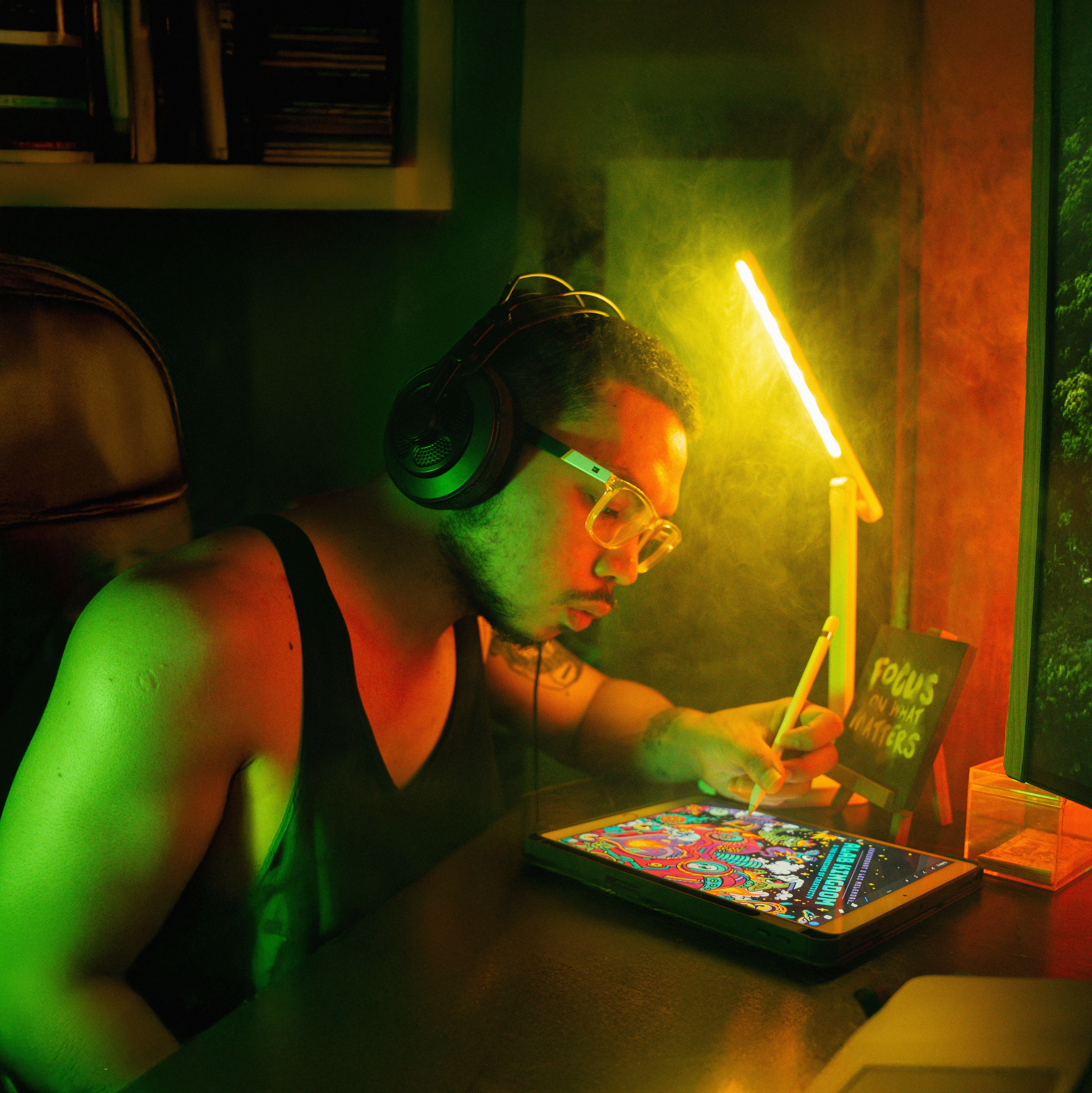 A focused digital artist using a tablet and stylus under colorful lighting, wearing headphones.