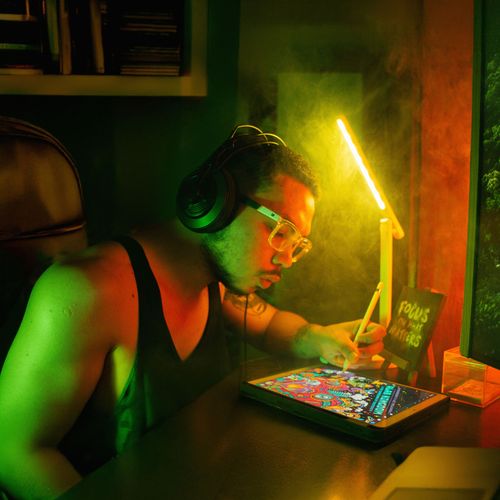 Free A focused digital artist using a tablet and stylus under colorful lighting, wearing headphones. Stock Photo