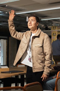 Person wearing a beige jacket raises hand in a modern office environment.