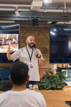 A lively speaker engages an audience at a workshop with two large screens in the background.