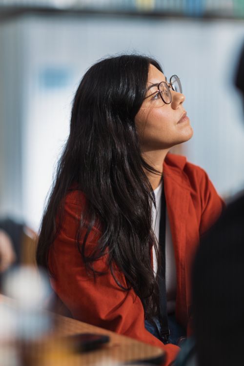 Free A thoughtful woman wearing glasses and a red jacket gazes upward in an indoor setting. Stock Photo