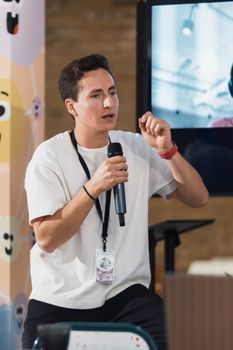 Man with microphone presenting at an indoor seminar with a projector screen.